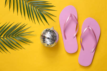 Disco ball with flip flops and palm leaves on yellow background. top view. flat lay. Minimalism beach party and rest conceptの写真素材