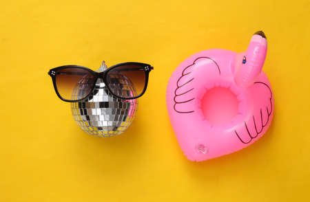 Inflatable flamingo with disco ball in sunglasses on yellow background. Minimalist party conceptの写真素材