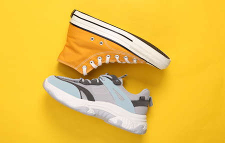 Two different sneakers on yellow pastel background. top viewの写真素材