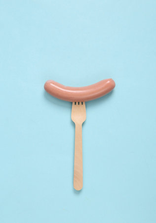 Sausage on a wooden fork. Minimalism food and eco concept. blue backgroundの写真素材