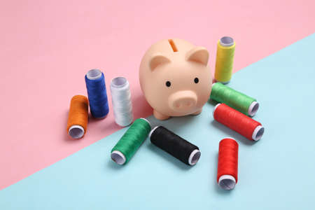 Piggy bank with Skeins of colored thread on a blue-pink pastel background