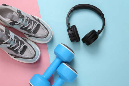 Sports shoes, headphones and dumbbells on blue-pink pastel background. fitness concept. top view....