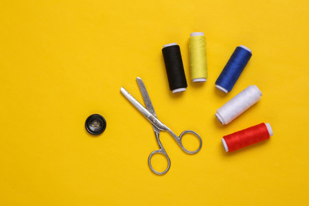 Skeins of colored thread, scissors and button on yellow backgroundの写真素材