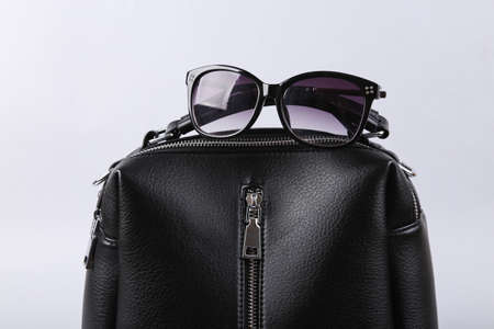 Stylish black leather handbag with sunglasses on gray background