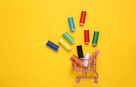 Shopping trolley with Skeins of colored thread on yellow backgroundの写真素材