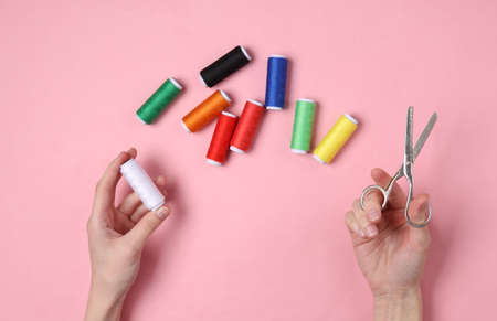 Hand holding Skeins of colored thread and scissors on pink pastel background