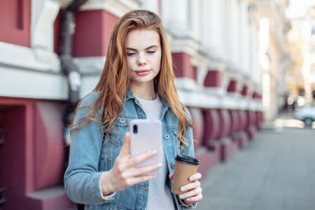 Young pretty woman using smartphone and holding a cup of coffee in the city