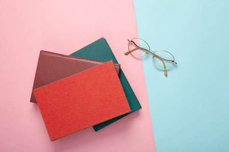 Stack of books and optical eyeglasses on blue pink pastel background