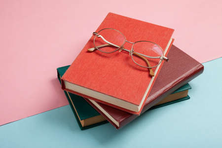 Stack of books and optical eyeglasses on blue pink pastel background