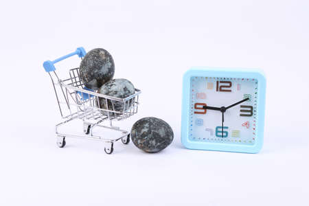 Mini supermarket trolley with Gray marble painted Easter eggs and alarm clock on white background