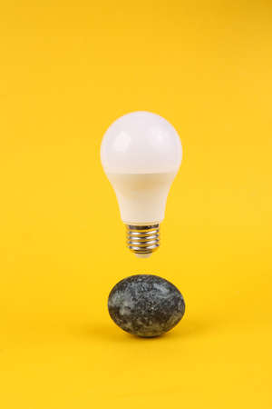 Gray marble painted Easter egg and floating light bulb on yellow background. Minimalistic Easter...