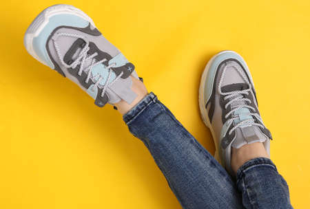 Female legs in fashionable jeans and sneakers on yellow background