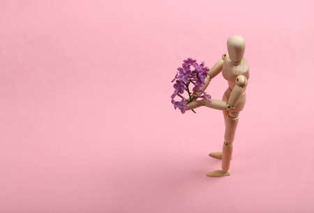 Wooden puppet holding a bouquet of blossoms on a pink background. Romantic, love conceptの写真素材