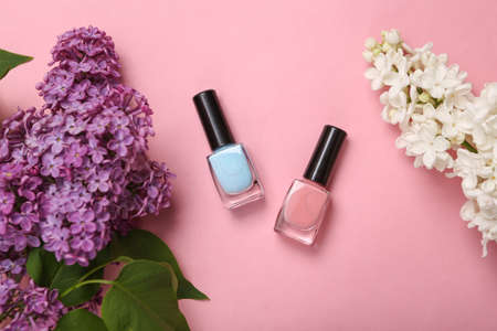 Nail polish bottles with branches of blooming lilacs on pink background. Spring beauty concept. top view. flat layの写真素材