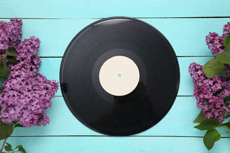 Vinyl record with branches of blooming lilacs on blue wooden background. music concept. top view....