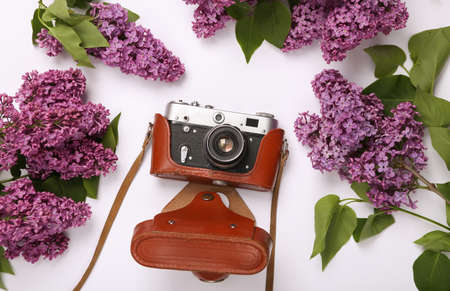 Retro camera with branches of blooming lilacs on white background. spring concept. top view. flat...