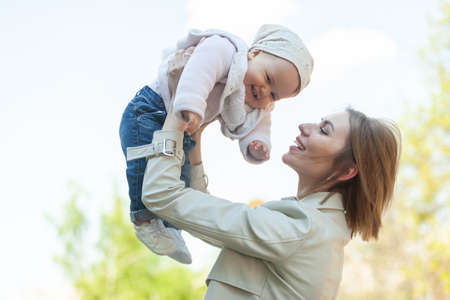 Loving Mom Raises Little Daughter Above Head Outdoorsの写真素材