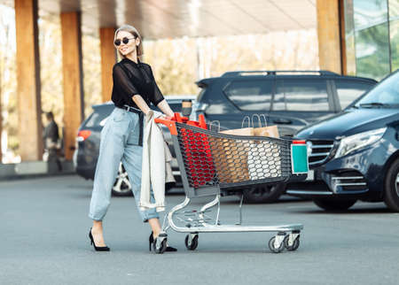 Stylish fashion lady with a shopping trolley on the background of a parking lot. lifestyleの写真素材