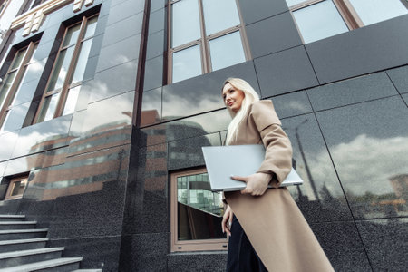 Stylish blonde business woman with laptop in trench coat in urban locationの写真素材
