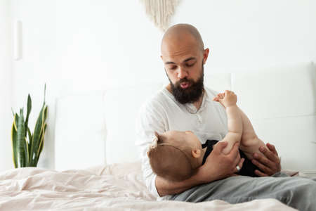Caring father plays with his little daughter on the bed in the bedroom. Love and care, happy family,...