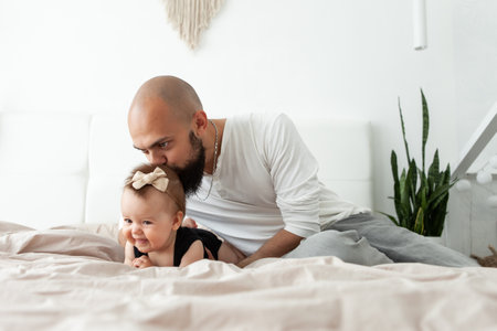 Caring father kisses his beautiful daughter on the head on the bed in the bedroom. Love and care, happy family conceptの写真素材