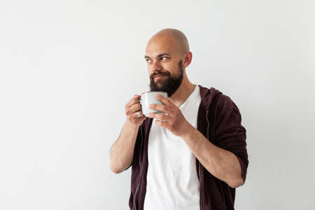 Young bearded smiling man holding a cup of tea or coffee on white background