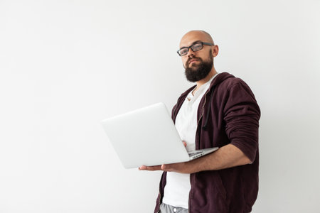 Confident bearded bald handsome male freelancer in glasses holding laptop on white backgroundの写真素材