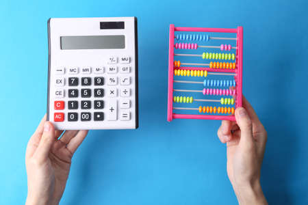 Hand holds children's colored abacus and calculator on blue backgroundの写真素材