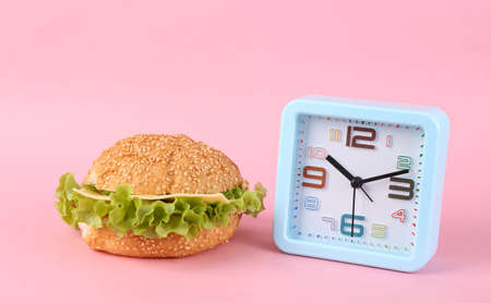 Appetizing burger and clock on a pink background. Diet conceptの写真素材