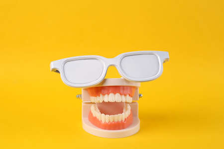 Minimal fun and party concept. Plastic model of a human jaw with white glasses on yellow backgroundの写真素材