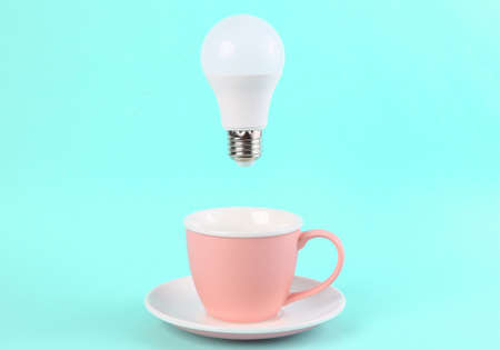 Cup with floating light bulb on a blue background. Minimal idea, inspiration conceptの写真素材