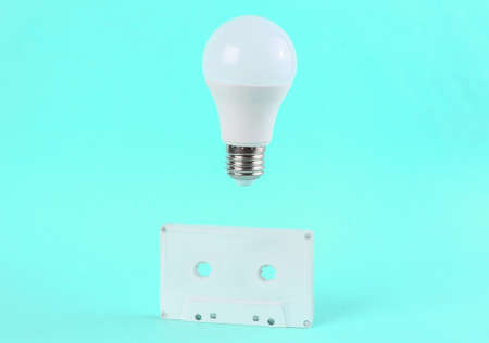 Retro audio cassette and floating light bulb on a bright blue background. Minimal concept art