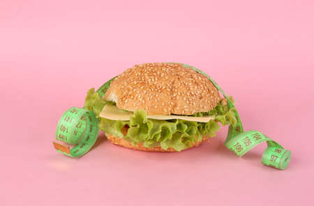 Appetizing burger with measuring tape on a pink background. weight loss conceptの写真素材