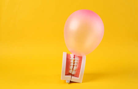The jaw model inflates a balloon or gum against a bright yellow background. Minimal fun concept