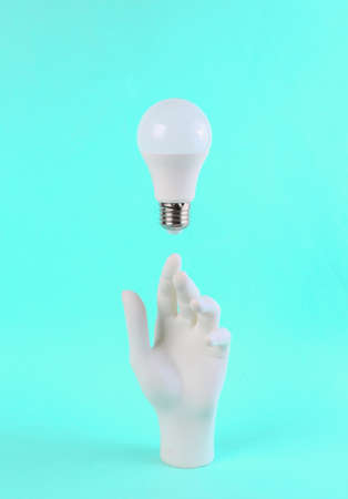 White hand and hovering light bulb on blue bright background. Minimal concept artの写真素材