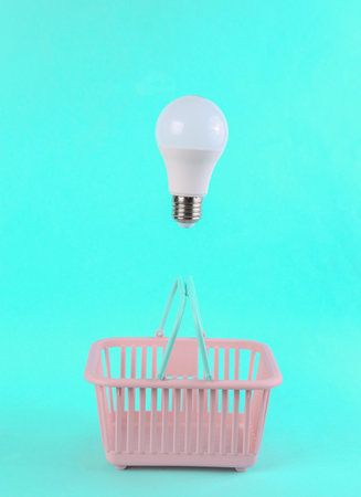 Shopping basket with floating light bulb on blue bright background. Minimal shopping conceptの写真素材