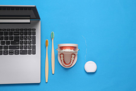 Dental care concept. Laptop, Jaw model with white teeth, wooden toothbrushes and dental floss on...