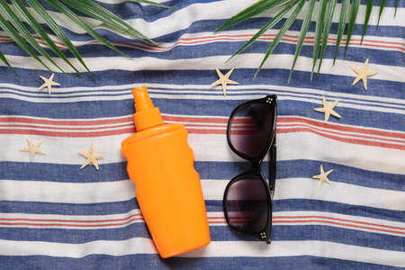 Sunblock bottle, sunglasses with starfish and palm leaves on striped surface. Beach vacation...