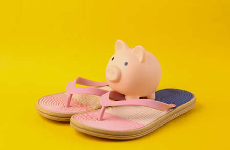 Colored flip flops with piggy bank on yellow background. Beach vacation concept.