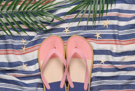 Flip flops with starfish and palm leaves on a striped surface. Beach vacation concept. flat lay