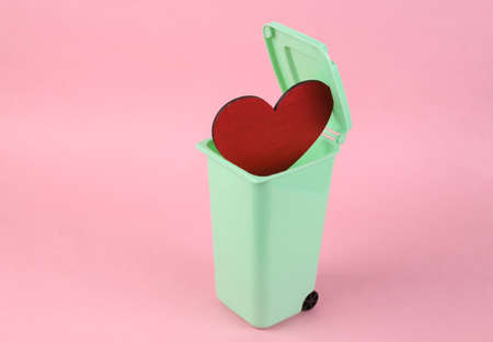 Broken heart concept. Red heart in trash can on pink backgroundの写真素材