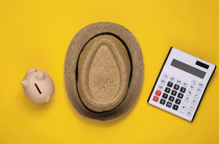 Straw hat and piggy bank with a calculator on a yellow background. Travel costsの写真素材
