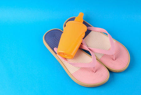 Colored flip flops with sunblock bottle on blue background. Beach vacation concept.