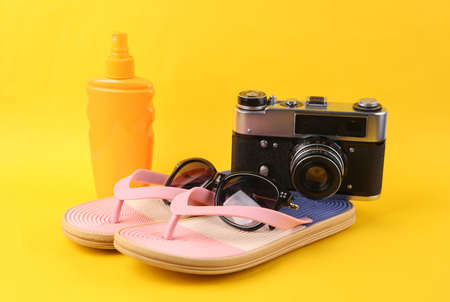 Colored flip flops with camera and sunblobk on yellow background. Beach vacation concept.の写真素材