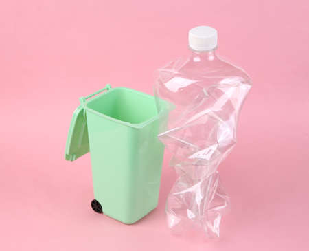 Plastic bottle and toy trash can on pink background. plastic recycling concept