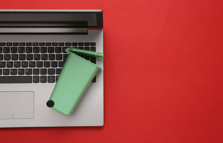 Cleaning your computer from debris. Laptop with miniature trash can on red background. Information trashの写真素材