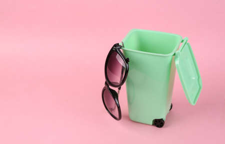 Trash can with plastic sunglasses on a pink background. Recycling conceptの写真素材
