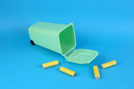 Battery recycling concept. Miniature trash can with aa batteries on blue background