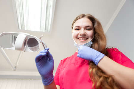 Woman doctor dentist holding down her face mask smilingly looks at the camera in dental officeの写真素材