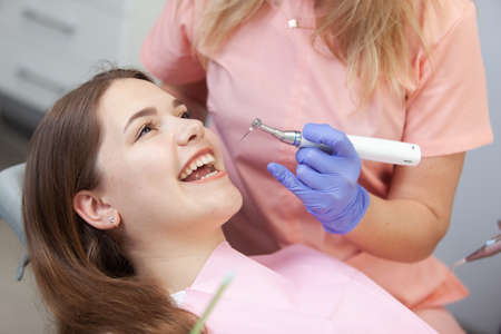 Dentists using dental drill while examining girl's mouth in clinic. Professional treatment at dental clinicの写真素材